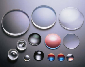 The image shows a collection of various lenses of different sizes and shapes. They appear to be made of clear glass or plastic, with some exhibiting a slight tint of color.  The lenses are arranged on a dark gray surface, showcasing their optical clarity and precision.  The overall impression is one of scientific precision and optical technology.
