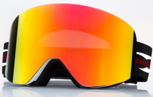 The image shows a pair of blue ski goggles. The lenses are a vibrant blue with a slight mirror effect, and the frame is a teal or light red color. A portion of a black strap with red lettering is visible. The goggles are displayed against a plain white background. 